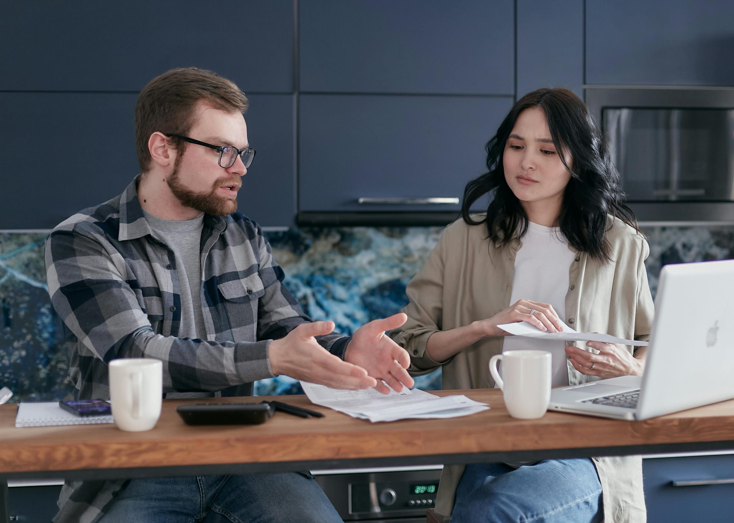 A young couple discusses financial documents at home, feeling stressed about budget concerns.